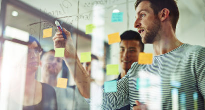 Cropped shot of coworkers using sticky notes on a glass wall during a meeting